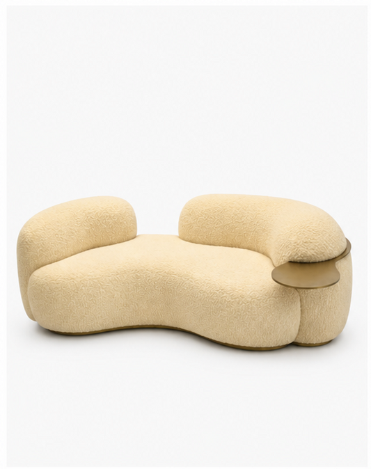 A modern, organic-shaped boucle sofa in a warm cream color, featuring a small round metallic side table attached to the right armrest, set against a plain white background.