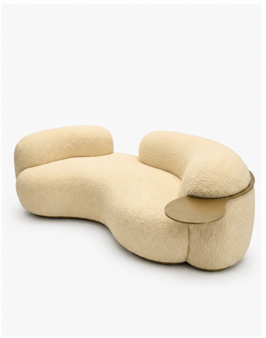 A modern curved upholstered lounge chair in a warm cream bouclé fabric with a small round metallic side table attached on the right side, shown on a clean white background.